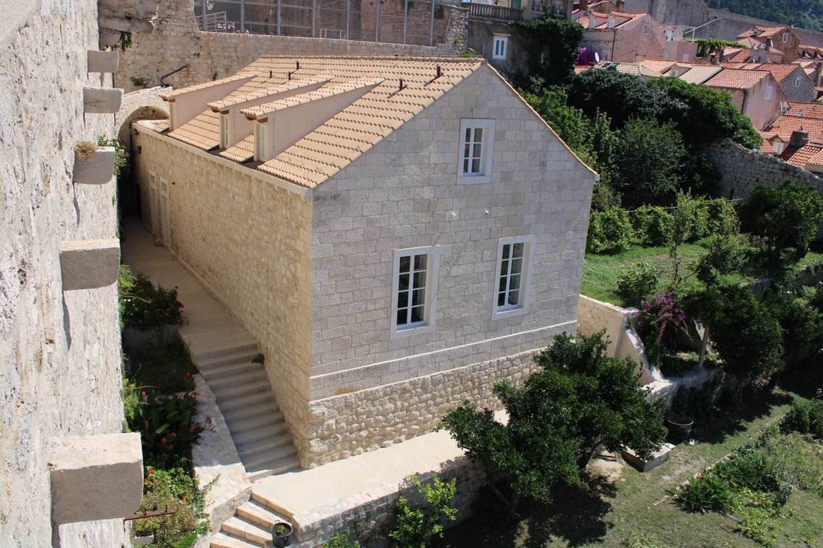 A stone house in a garden below the wall